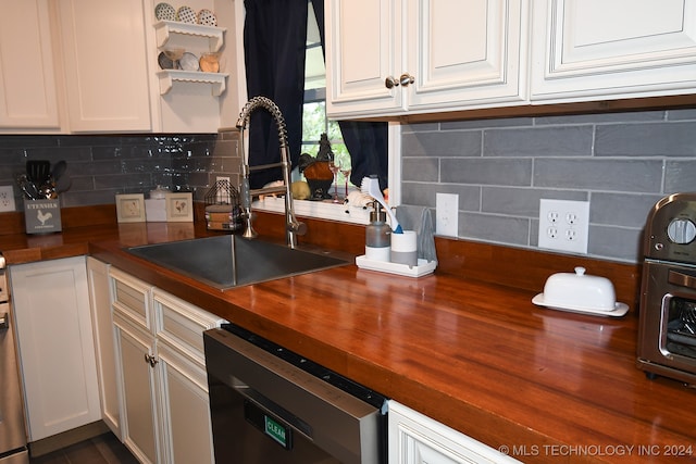 kitchen with dishwasher, wooden counters, sink, and white cabinetry