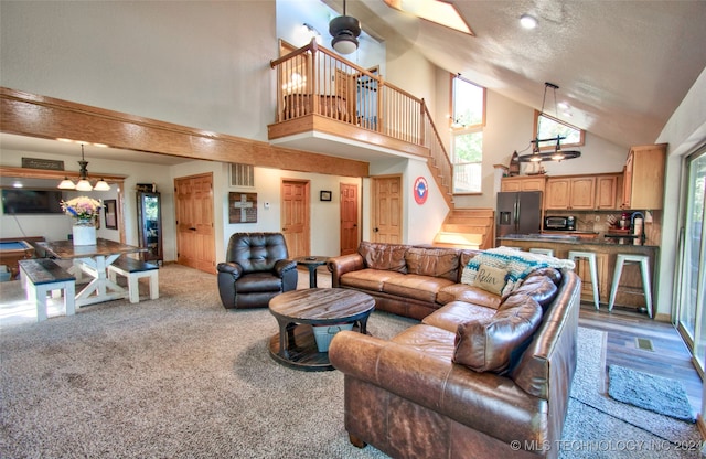 living room with a textured ceiling, carpet floors, high vaulted ceiling, and ceiling fan