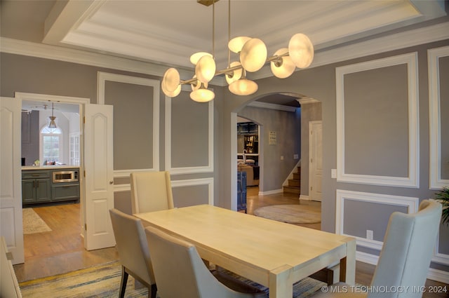 dining space featuring crown molding, light wood-type flooring, and a tray ceiling