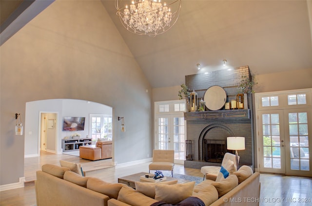 living room featuring a fireplace, high vaulted ceiling, light hardwood / wood-style flooring, an inviting chandelier, and french doors