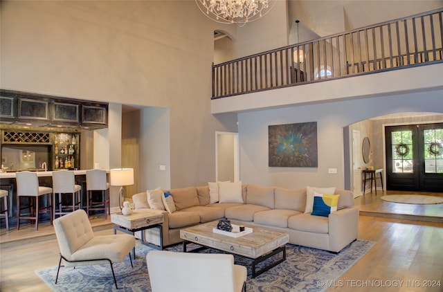 living room with a towering ceiling, wood-type flooring, indoor bar, and a notable chandelier