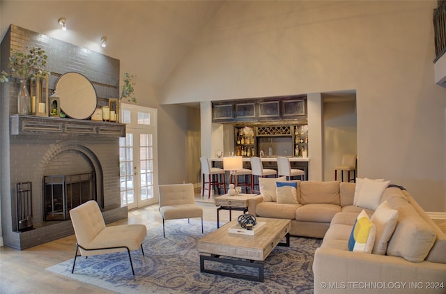 living room with bar area, high vaulted ceiling, a brick fireplace, and hardwood / wood-style flooring