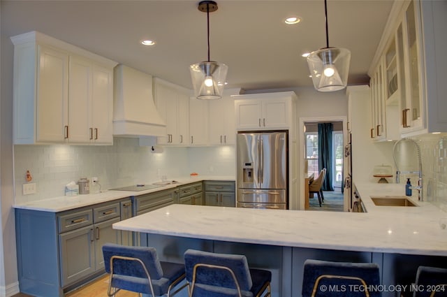 kitchen featuring stainless steel fridge, custom range hood, gray cabinetry, and hanging light fixtures