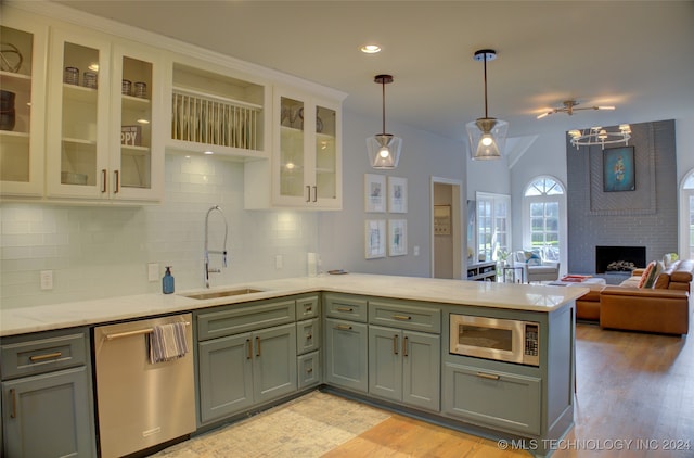 kitchen with a fireplace, appliances with stainless steel finishes, hanging light fixtures, sink, and light wood-type flooring