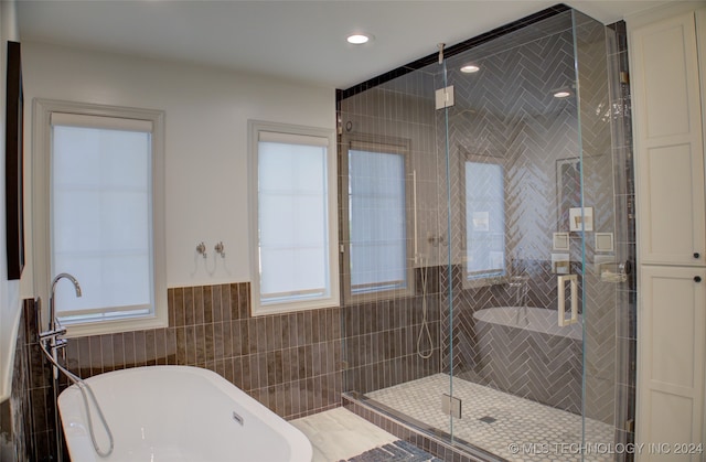 bathroom featuring plenty of natural light, shower with separate bathtub, and tile walls