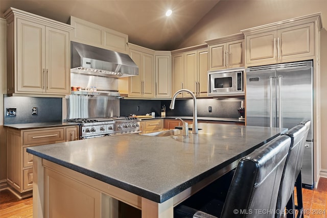 kitchen with ventilation hood, cream cabinets, lofted ceiling, built in appliances, and a center island with sink