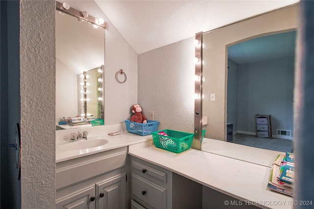 bathroom featuring a textured wall, vanity, visible vents, and vaulted ceiling