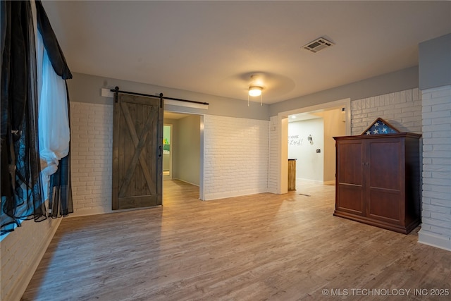 spare room featuring a barn door, brick wall, and light hardwood / wood-style floors