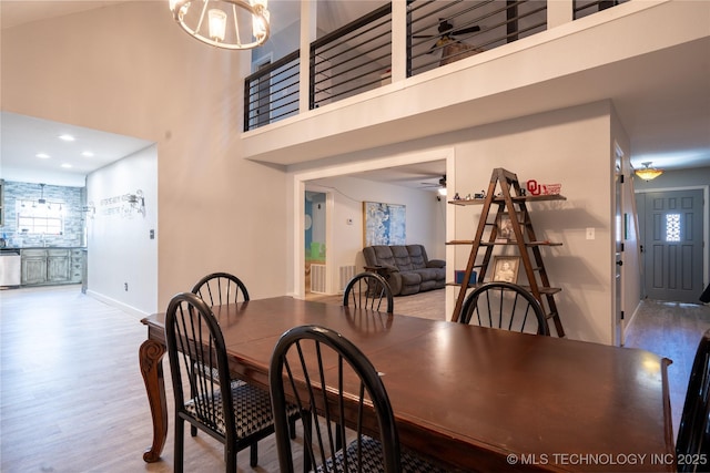 dining area with a high ceiling, ceiling fan with notable chandelier, and light hardwood / wood-style floors