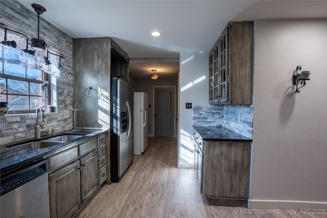 kitchen featuring decorative light fixtures, stainless steel appliances, sink, backsplash, and light wood-type flooring