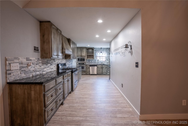 kitchen with tasteful backsplash, dark stone countertops, custom exhaust hood, light hardwood / wood-style flooring, and appliances with stainless steel finishes