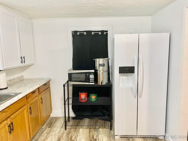 kitchen with a textured ceiling, light wood-type flooring, white fridge with ice dispenser, and white cabinets