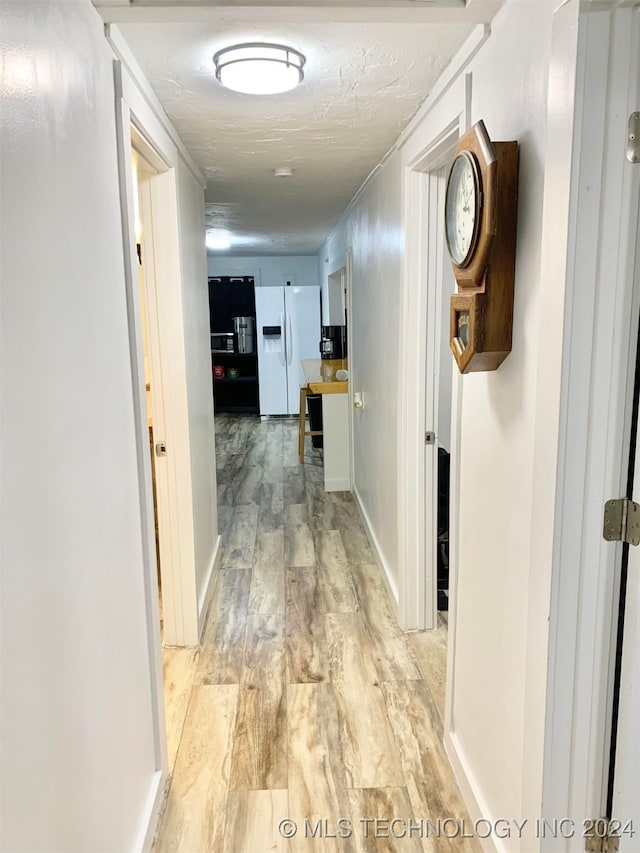 corridor with light hardwood / wood-style floors and a textured ceiling