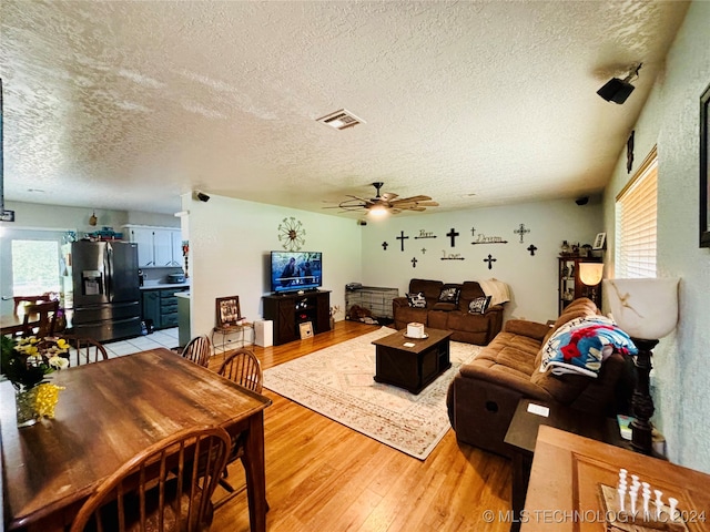 living room featuring ceiling fan, plenty of natural light, a textured ceiling, and light wood-type flooring