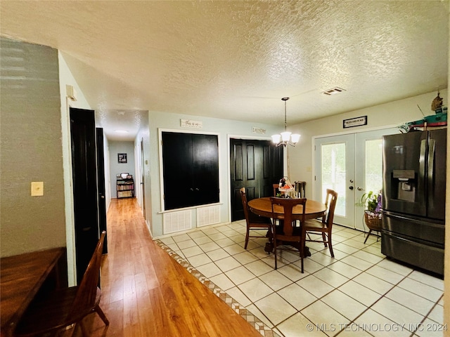 dining room featuring french doors, a chandelier, a textured ceiling, and light wood-type flooring