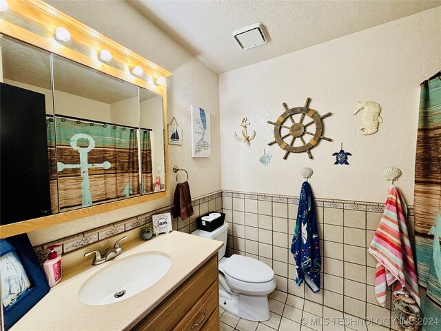 bathroom with vanity, tile patterned flooring, toilet, tile walls, and a textured ceiling