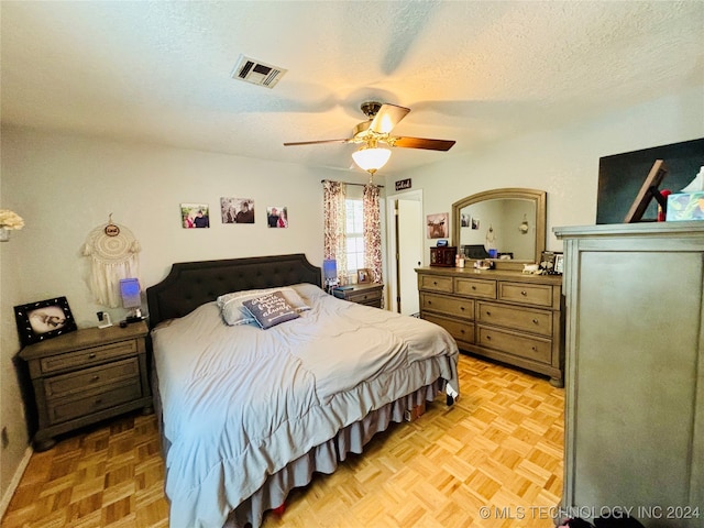 bedroom featuring ceiling fan, light parquet floors, and a textured ceiling