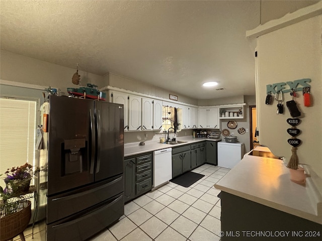 kitchen with white dishwasher, black fridge, sink, light tile patterned floors, and white cabinetry