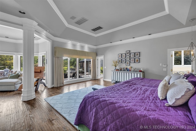 bedroom featuring wood-type flooring, a tray ceiling, and decorative columns