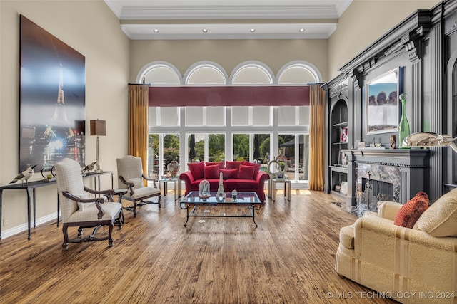 living room with wood-type flooring, a high ceiling, ornamental molding, and a premium fireplace