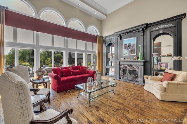 living room with a high ceiling, a fireplace, ornamental molding, and hardwood / wood-style floors