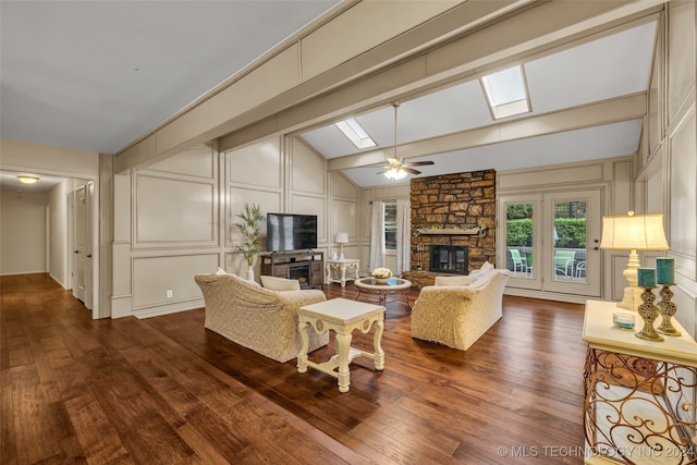 living room featuring dark wood-type flooring, ceiling fan, vaulted ceiling with skylight, and a fireplace