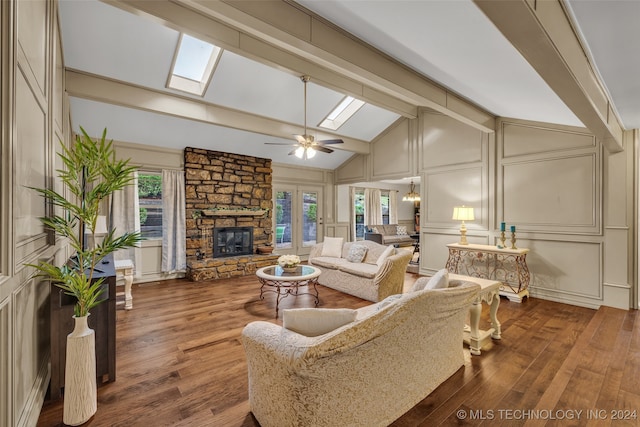 living room with a stone fireplace, ceiling fan, vaulted ceiling with skylight, ornamental molding, and dark hardwood / wood-style floors