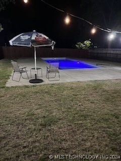 pool at night featuring a yard and a patio area