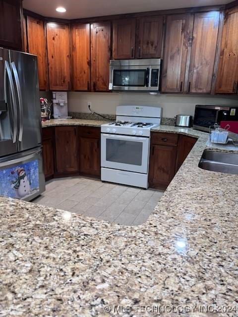 kitchen featuring fridge, sink, light stone countertops, and white gas stove