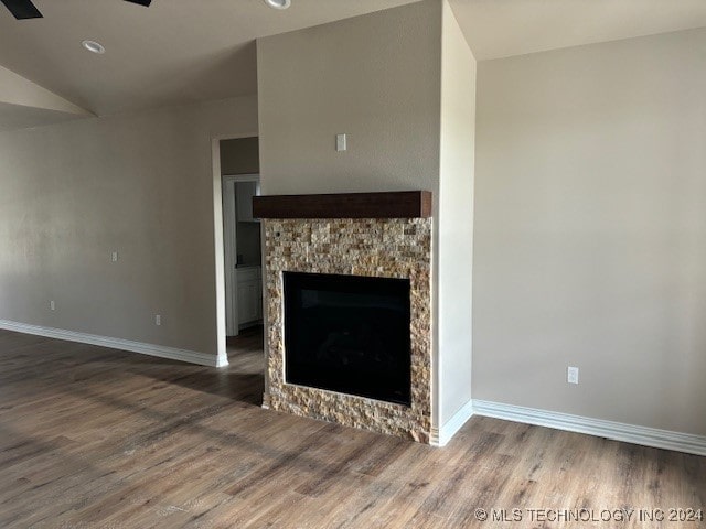 unfurnished living room featuring lofted ceiling, a fireplace, baseboards, and wood finished floors