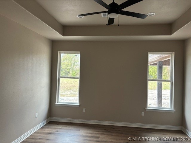 empty room with a ceiling fan, a tray ceiling, baseboards, and wood finished floors