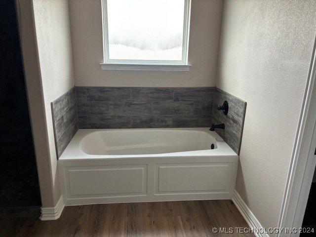 bathroom featuring wood finished floors, a bath, and baseboards