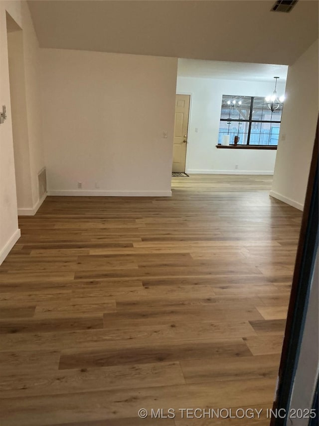 unfurnished room featuring baseboards, wood finished floors, visible vents, and an inviting chandelier