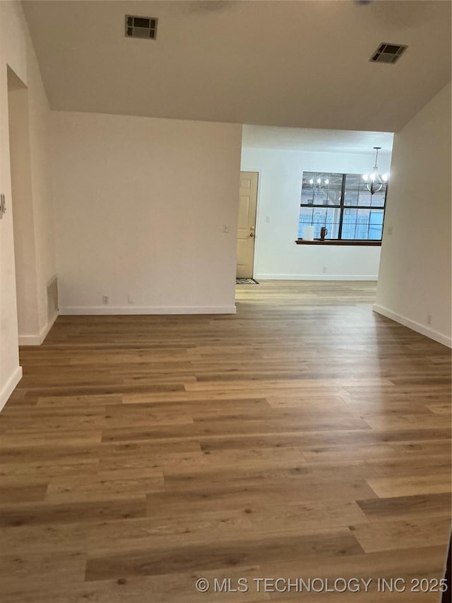 spare room with wood finished floors, visible vents, and an inviting chandelier