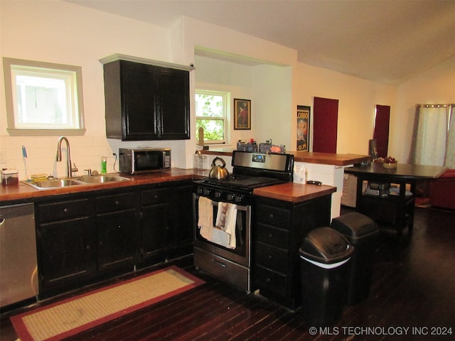 kitchen with dark wood-type flooring, sink, kitchen peninsula, decorative backsplash, and appliances with stainless steel finishes