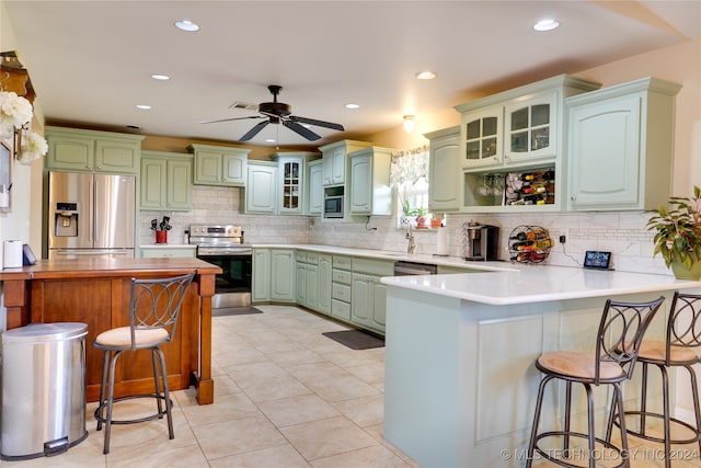 kitchen with a breakfast bar area, kitchen peninsula, green cabinets, appliances with stainless steel finishes, and ceiling fan