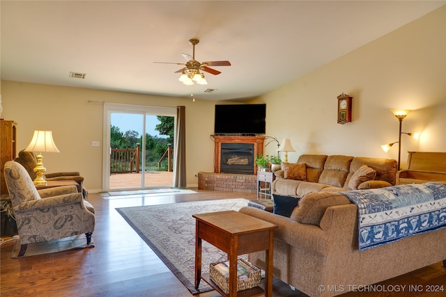 living room featuring a brick fireplace, ceiling fan, and dark wood-type flooring