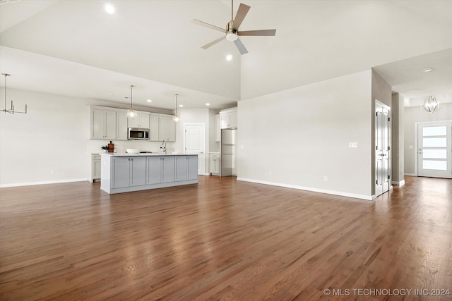 unfurnished living room featuring ceiling fan with notable chandelier, high vaulted ceiling, dark wood-type flooring, and sink