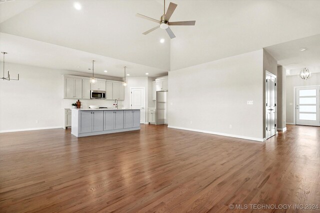 unfurnished living room featuring ceiling fan with notable chandelier, high vaulted ceiling, dark wood-type flooring, and sink