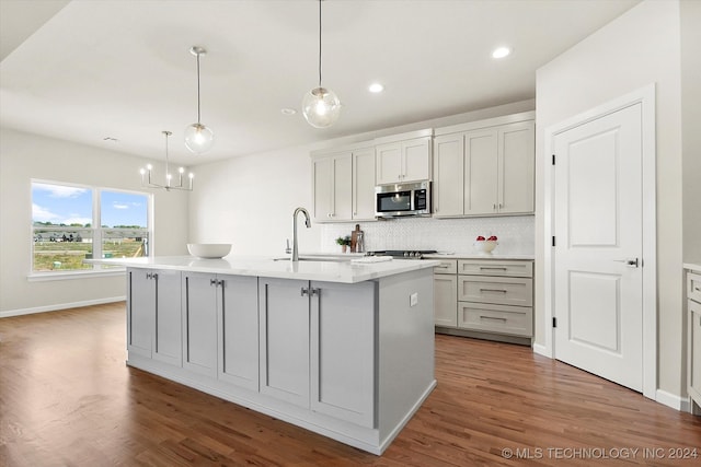 kitchen featuring an island with sink, hanging light fixtures, sink, and hardwood / wood-style floors