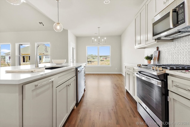 kitchen featuring hanging light fixtures, dark wood-type flooring, white cabinets, stainless steel appliances, and a center island with sink