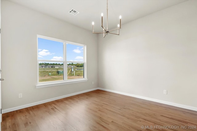 empty room with wood-type flooring and an inviting chandelier