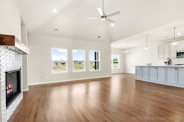 unfurnished living room with a tile fireplace, a wealth of natural light, ceiling fan with notable chandelier, and hardwood / wood-style flooring