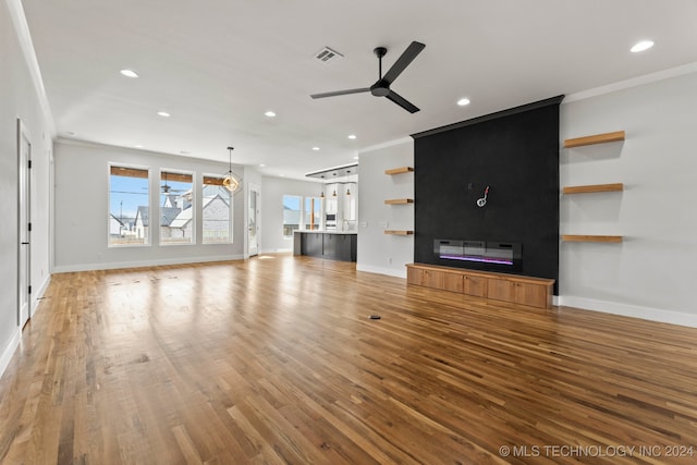 unfurnished living room with light wood-type flooring, ceiling fan, a large fireplace, and crown molding