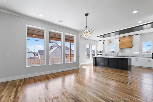 kitchen featuring an island with sink, white cabinets, a healthy amount of sunlight, and decorative light fixtures