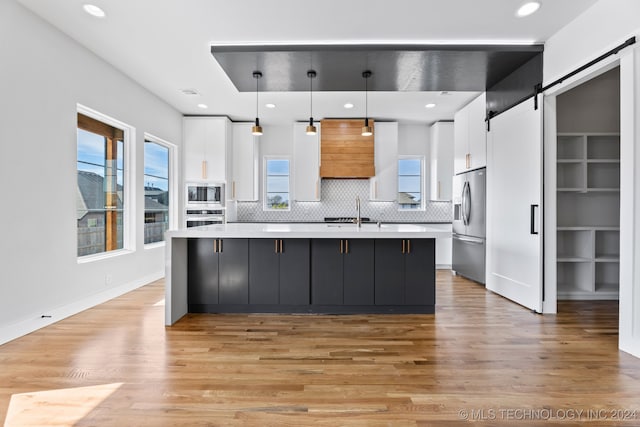 kitchen featuring white cabinets, hanging light fixtures, appliances with stainless steel finishes, a barn door, and a healthy amount of sunlight