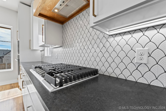 kitchen featuring wood-type flooring, decorative backsplash, stovetop, and white cabinets