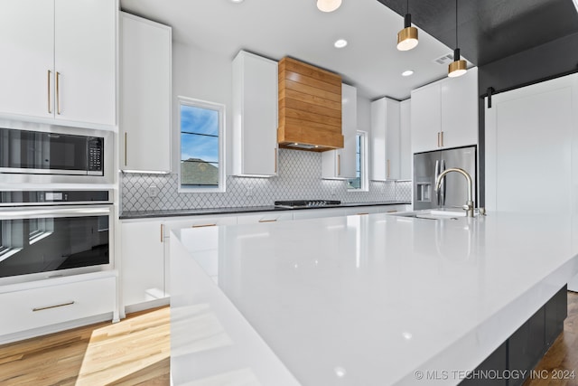 kitchen featuring hanging light fixtures, white cabinetry, a barn door, stainless steel appliances, and sink