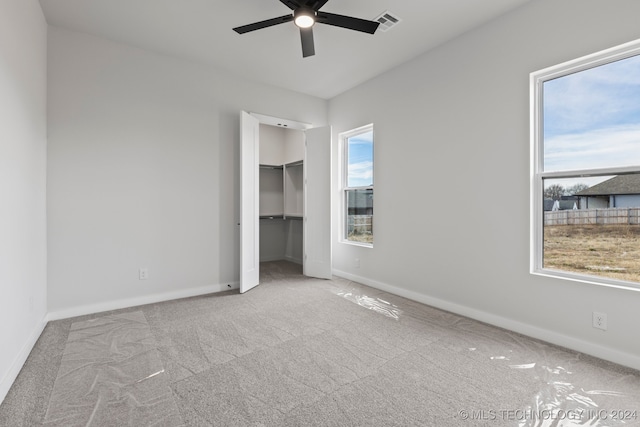 unfurnished bedroom featuring a spacious closet, light carpet, ceiling fan, and a closet