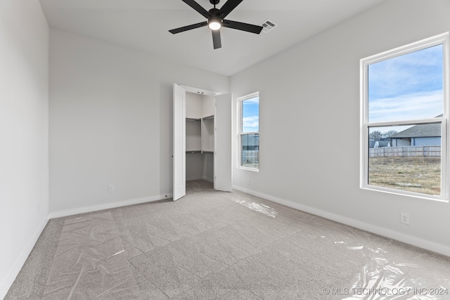 unfurnished bedroom featuring a spacious closet, light carpet, ceiling fan, and a closet